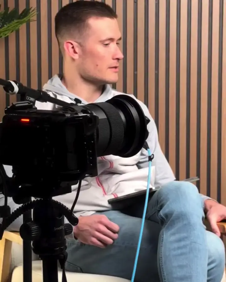 Podcast guest seated in front of a wood slat wall with a camera in the foreground