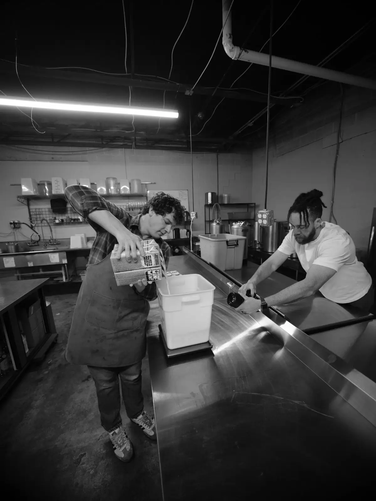Tyler Thompson filming a chef pouring at the counter of a commercial kitchen, in black and white