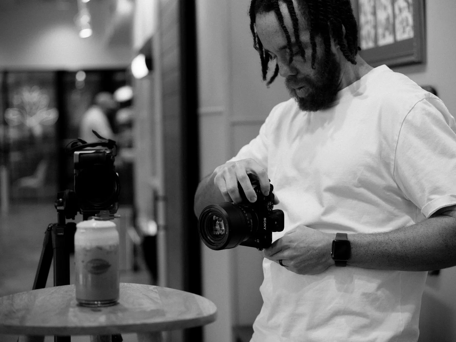 Tyler Thompson fitting a lens on a camera beside a tripod, in black and white