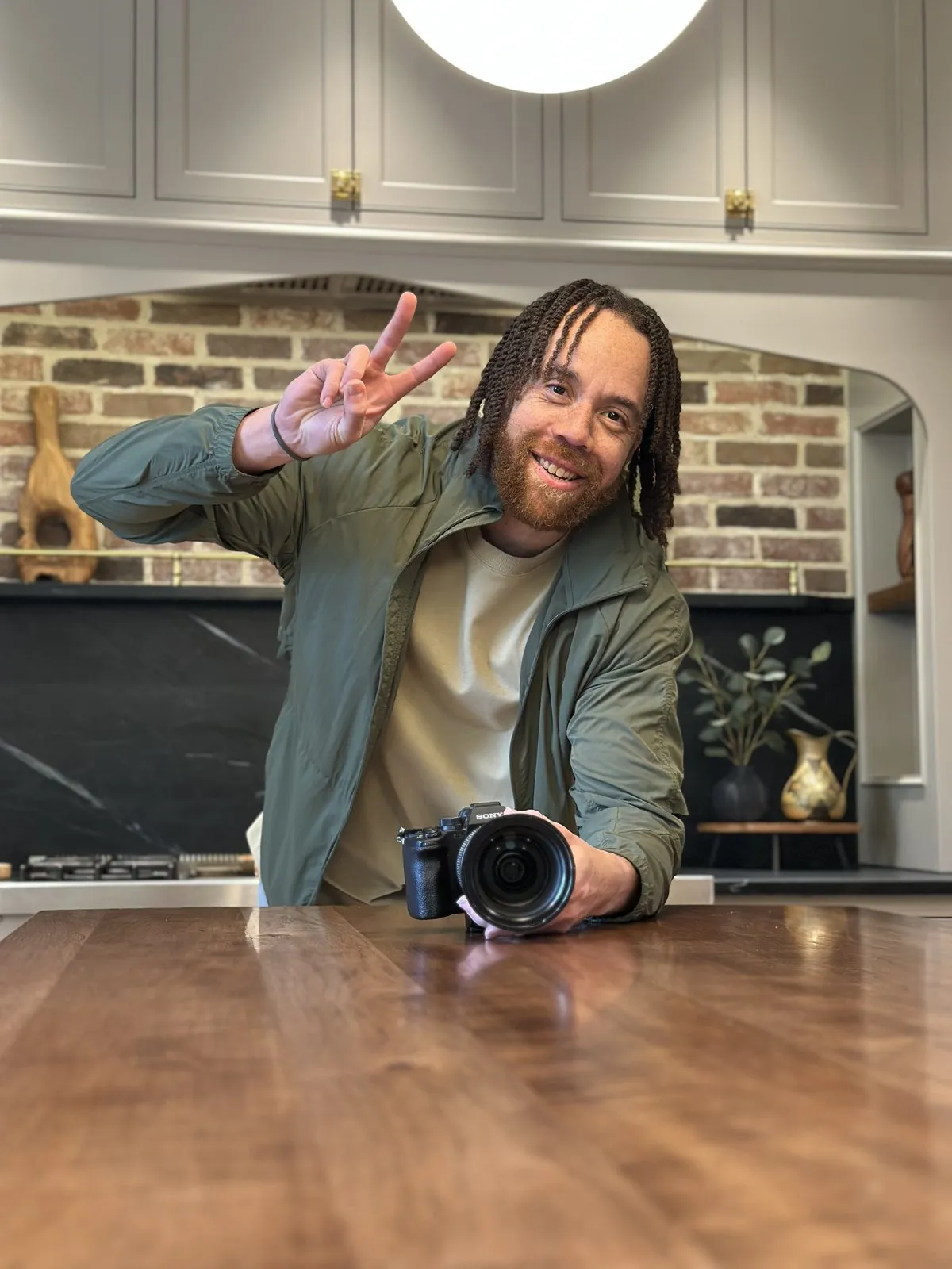 Tyler Thompson smiling and holding up a peace sign, a camera on the table in front of him