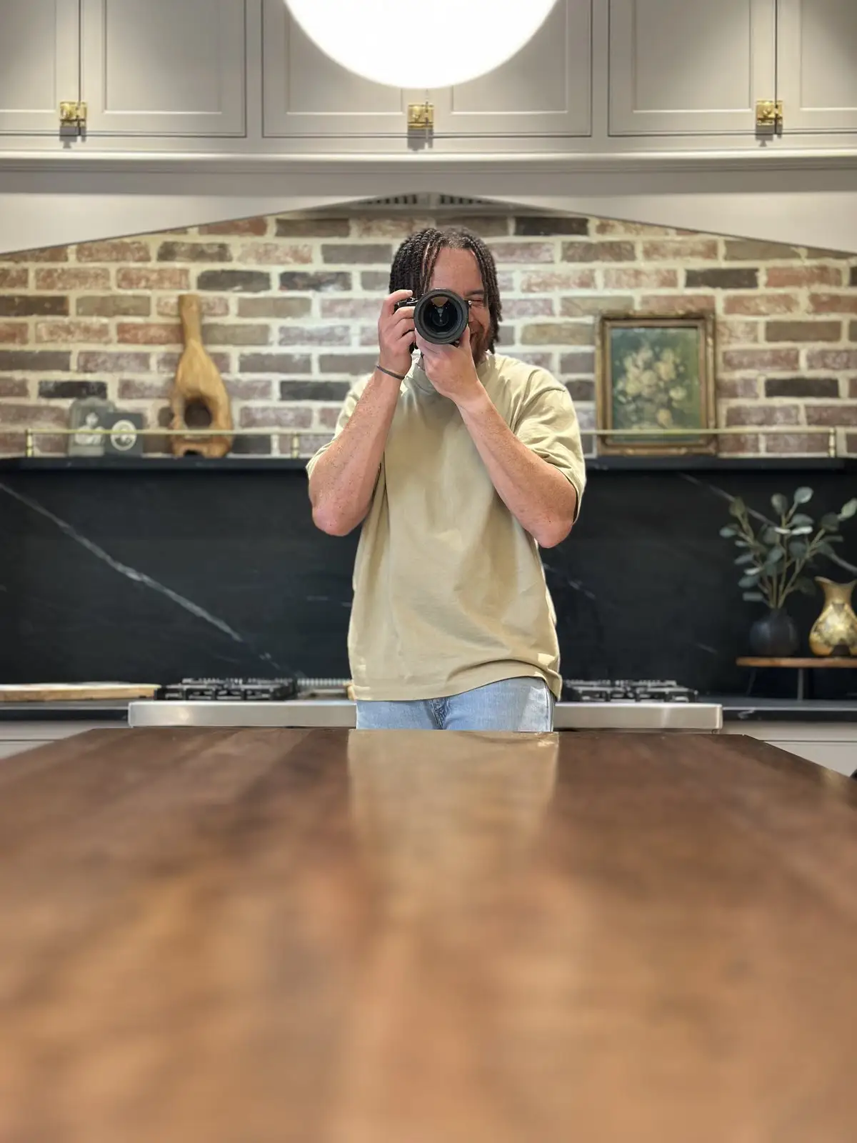 Tyler Thompson framing a shot with a camera held to his eye in front of a brick wall